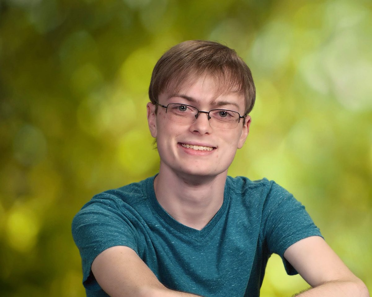 Portrait of Jacob in a teal t-shirt in front of a soft green background.
